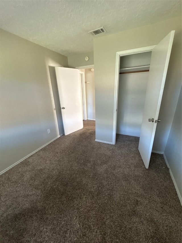 unfurnished bedroom with a closet, a textured ceiling, and dark colored carpet