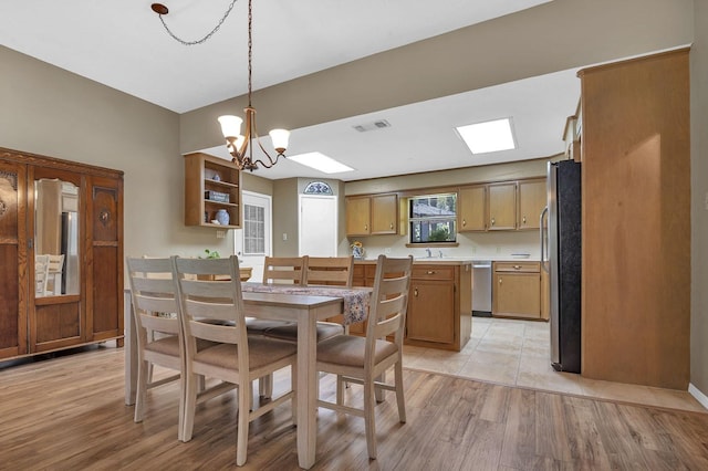 dining room with an inviting chandelier, a skylight, sink, and light hardwood / wood-style flooring