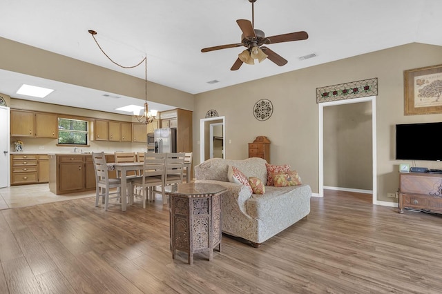 living room with lofted ceiling with skylight, light hardwood / wood-style flooring, ceiling fan with notable chandelier, and sink