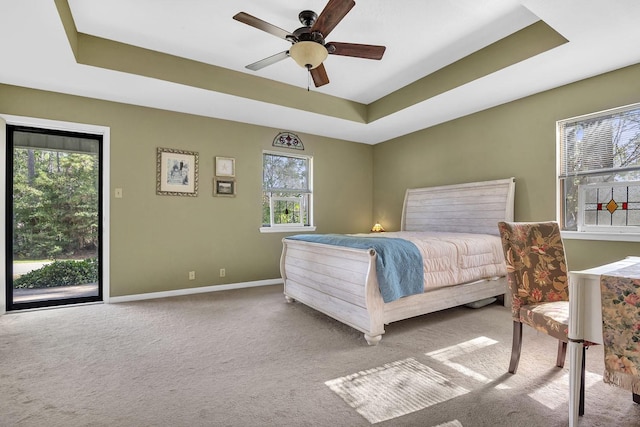 carpeted bedroom with access to exterior, a tray ceiling, and ceiling fan