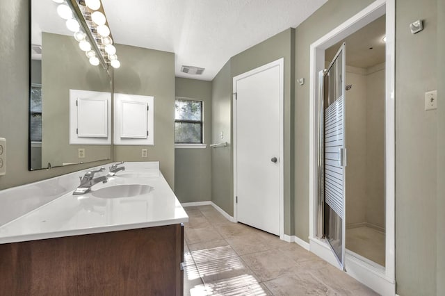 bathroom with tile patterned flooring, vanity, a shower with door, and a textured ceiling