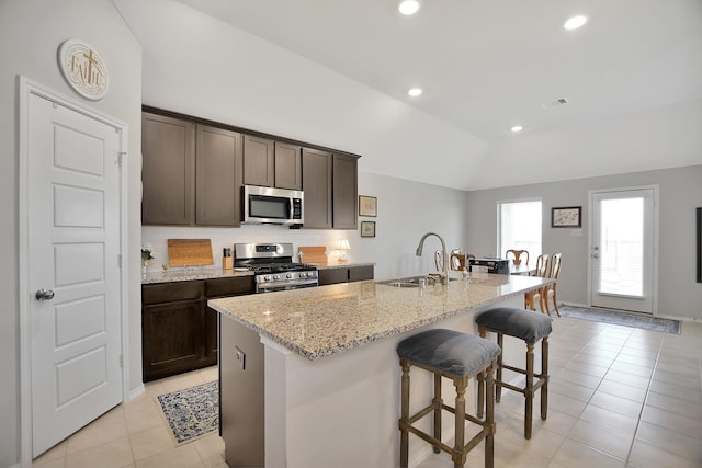 kitchen featuring a center island with sink, sink, vaulted ceiling, light stone countertops, and appliances with stainless steel finishes