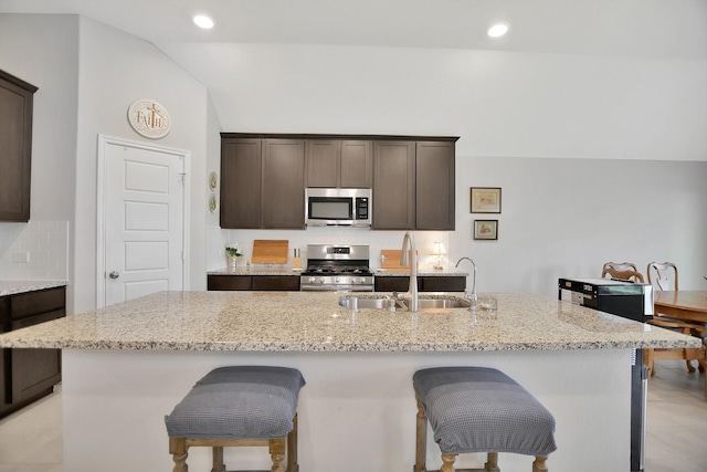 kitchen featuring light stone counters, a center island with sink, dark brown cabinets, and appliances with stainless steel finishes