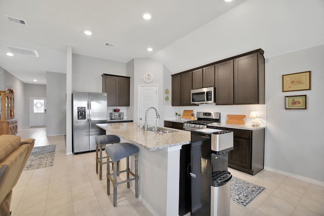 kitchen featuring appliances with stainless steel finishes, dark brown cabinetry, vaulted ceiling, sink, and a center island with sink