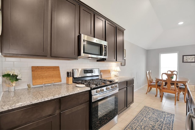 kitchen with light stone countertops, decorative backsplash, dark brown cabinetry, stainless steel appliances, and vaulted ceiling