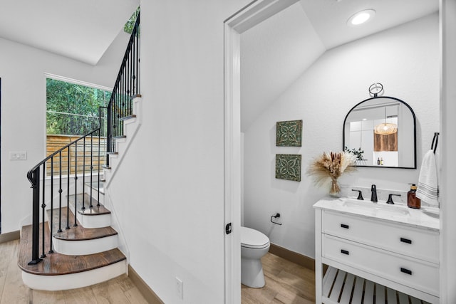 bathroom with vanity, toilet, wood-type flooring, and vaulted ceiling