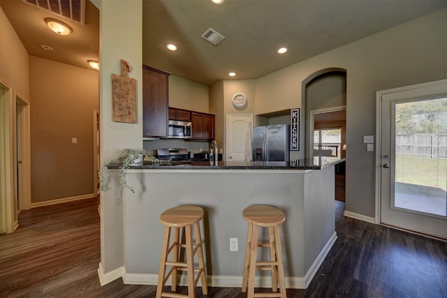 kitchen featuring kitchen peninsula, dark wood-type flooring, stainless steel appliances, and a breakfast bar