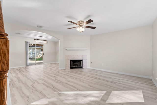 unfurnished living room with light wood-type flooring, ceiling fan, and a tiled fireplace