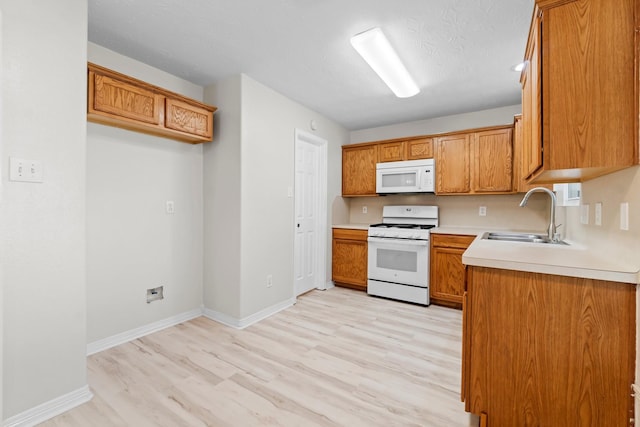 kitchen featuring a textured ceiling, light wood-type flooring, white appliances, and sink