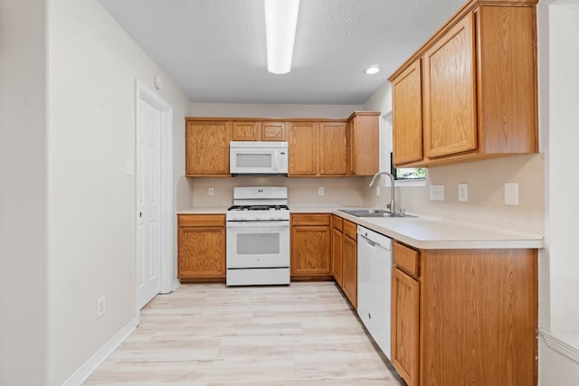 kitchen with a textured ceiling, white appliances, sink, and light hardwood / wood-style flooring