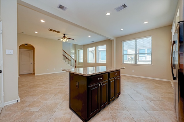 kitchen featuring ceiling fan, a kitchen island, dark brown cabinetry, and light tile patterned floors