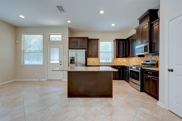 kitchen featuring light stone countertops, a center island, sink, tasteful backsplash, and appliances with stainless steel finishes