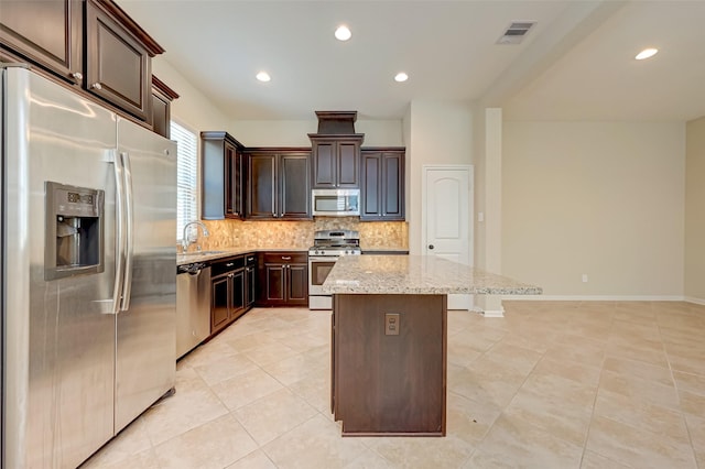 kitchen with light stone countertops, appliances with stainless steel finishes, dark brown cabinets, light tile patterned floors, and a center island