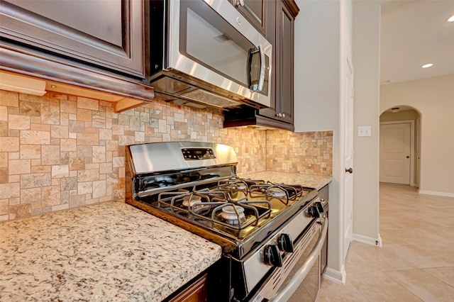 kitchen with decorative backsplash, light stone countertops, light tile patterned floors, appliances with stainless steel finishes, and dark brown cabinets