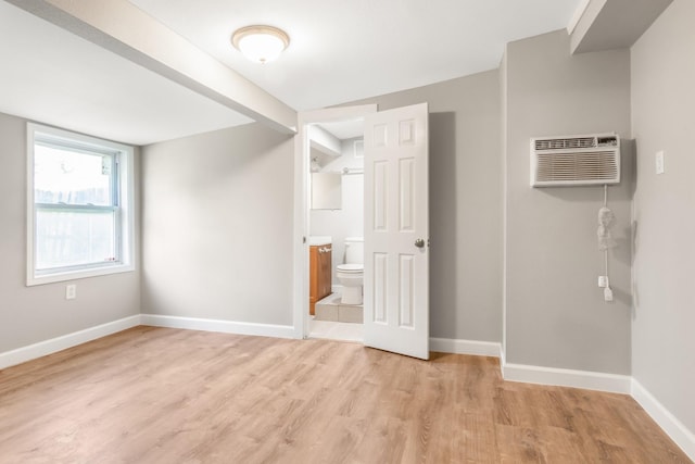 unfurnished bedroom with ensuite bathroom, light hardwood / wood-style flooring, and a wall mounted AC