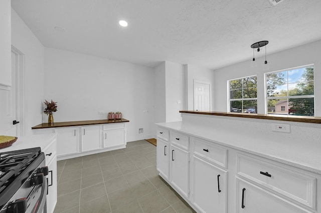 kitchen with light tile patterned floors, a textured ceiling, stainless steel stove, and white cabinetry