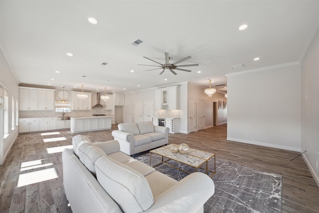 living room with hardwood / wood-style floors, ceiling fan with notable chandelier, crown molding, and sink