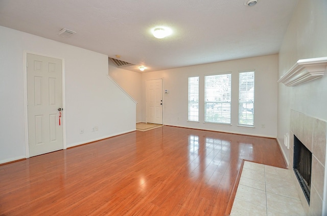 unfurnished living room with a tile fireplace, a textured ceiling, and light wood-type flooring