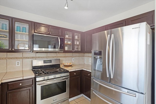 kitchen with decorative backsplash, light tile patterned floors, stainless steel appliances, and dark brown cabinets