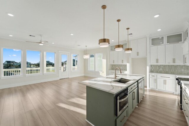 kitchen with white cabinetry, sink, light stone countertops, hanging light fixtures, and an island with sink