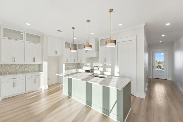 kitchen featuring a kitchen island with sink, sink, hanging light fixtures, light hardwood / wood-style floors, and white cabinetry