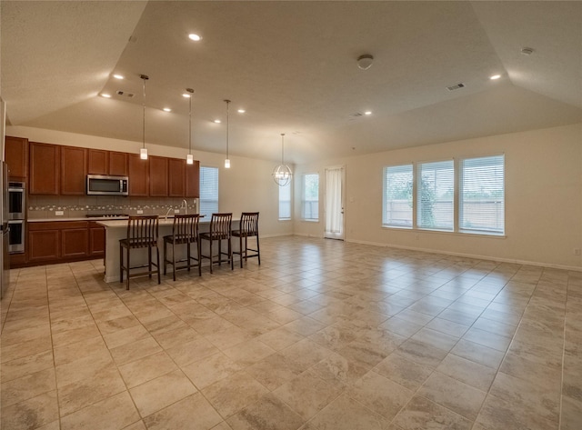 kitchen featuring tasteful backsplash, vaulted ceiling, decorative light fixtures, a center island with sink, and a breakfast bar area