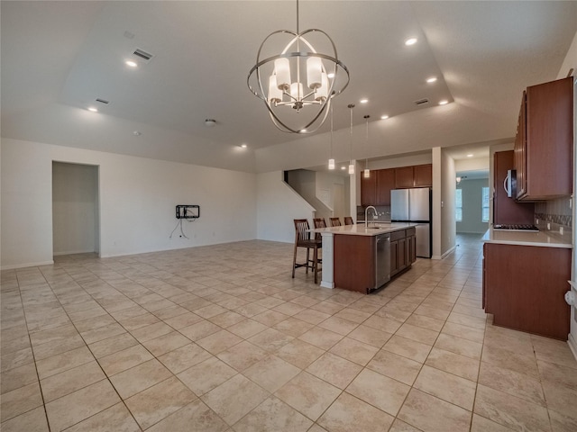 kitchen with stainless steel appliances, a raised ceiling, decorative light fixtures, an inviting chandelier, and an island with sink