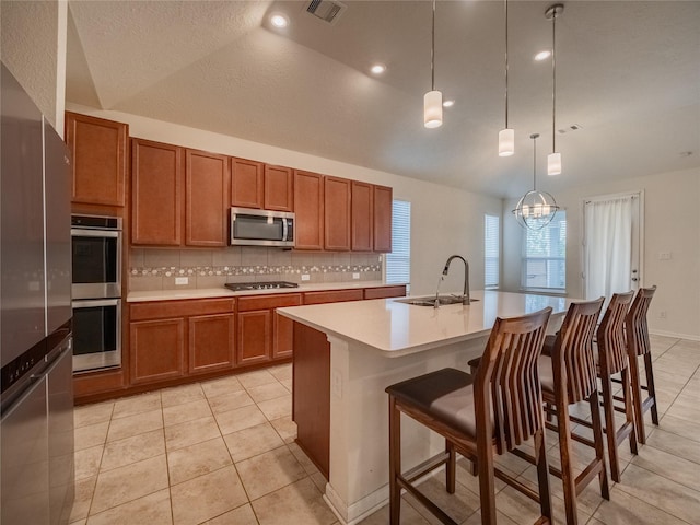 kitchen with a breakfast bar, lofted ceiling, sink, an island with sink, and stainless steel appliances