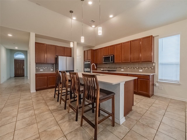 kitchen featuring tasteful backsplash, a kitchen island with sink, a breakfast bar, and decorative light fixtures