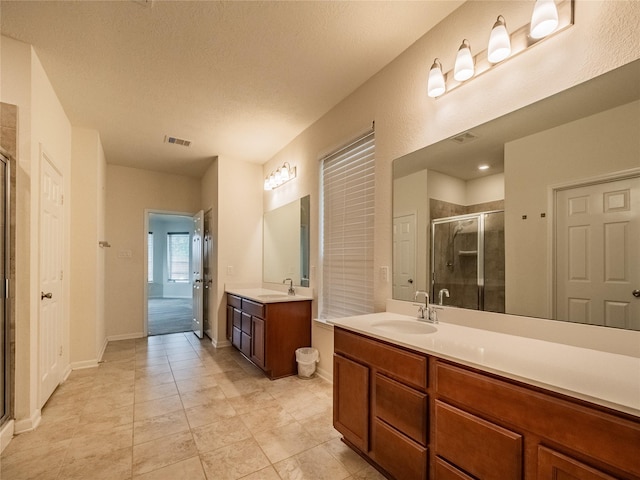 bathroom with a shower with door, vanity, a textured ceiling, and tile patterned flooring