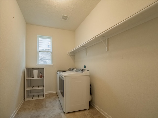 clothes washing area featuring light tile patterned floors, a textured ceiling, and washer and clothes dryer