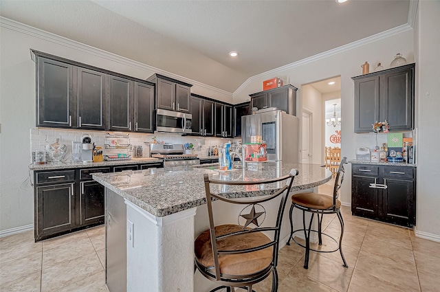 kitchen with light stone countertops, appliances with stainless steel finishes, backsplash, crown molding, and an island with sink