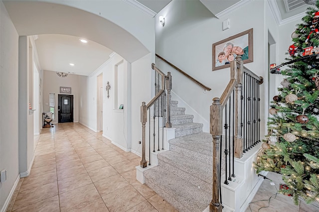 entryway with light tile patterned floors, a towering ceiling, and ornamental molding