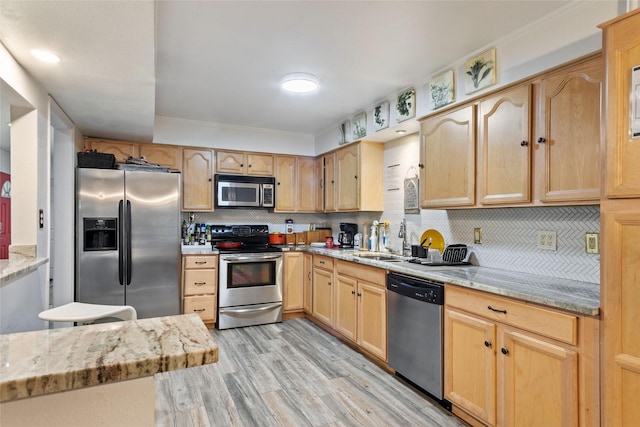 kitchen with light brown cabinets, sink, light stone countertops, light hardwood / wood-style floors, and stainless steel appliances