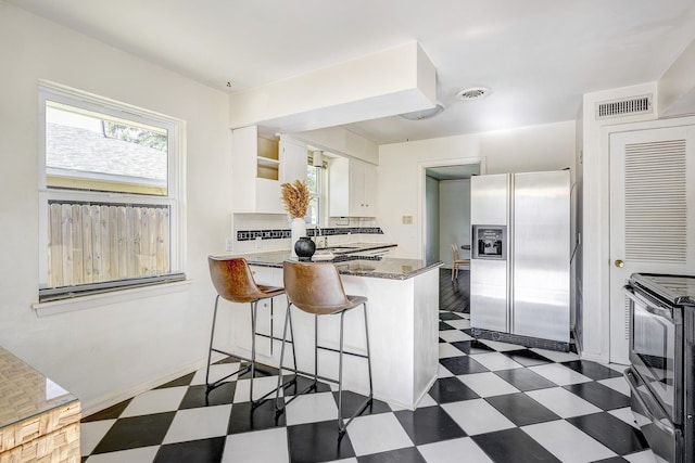 kitchen featuring kitchen peninsula, stainless steel appliances, white cabinetry, and dark stone countertops