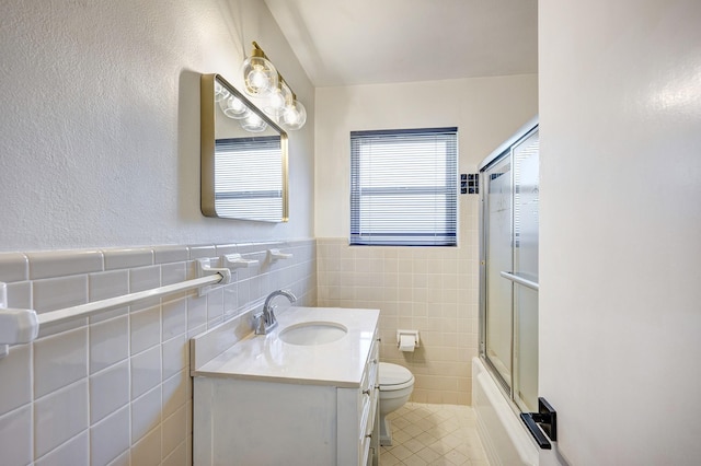 full bathroom with vanity, toilet, bath / shower combo with glass door, and tile walls