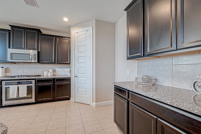 kitchen with light stone counters, backsplash, dark brown cabinets, light tile patterned floors, and appliances with stainless steel finishes