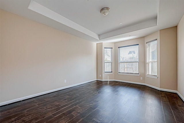 empty room with a tray ceiling and dark hardwood / wood-style flooring