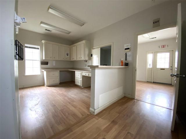 kitchen featuring kitchen peninsula, light wood-type flooring, white cabinetry, and built in desk