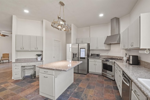 kitchen featuring wall chimney exhaust hood, stainless steel appliances, ceiling fan, decorative light fixtures, and a center island