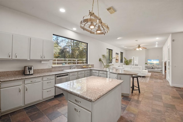 kitchen featuring pendant lighting, a center island, stainless steel dishwasher, ceiling fan, and light stone countertops