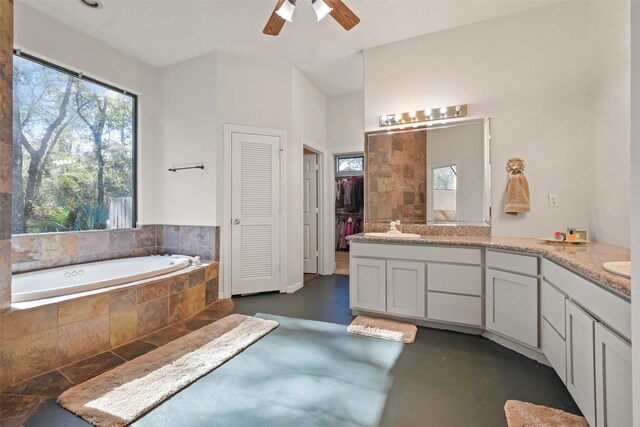 bathroom with vanity, tiled bath, ceiling fan, and concrete floors