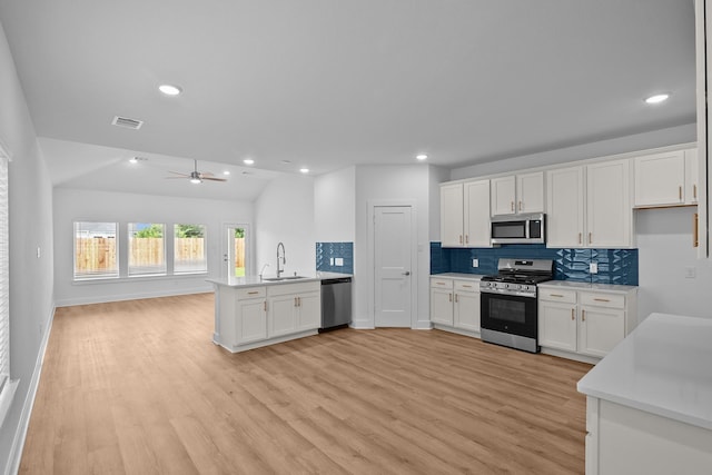31915 Splendor Dr, Fulshear, TX 77441 - kitchen featuring appliances with stainless steel finishes, a sink, open floor plan, backsplash, and light wood-style flooring