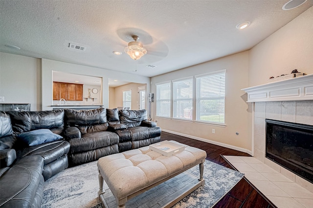 living room with a tile fireplace, ceiling fan, a textured ceiling, and light wood-type flooring