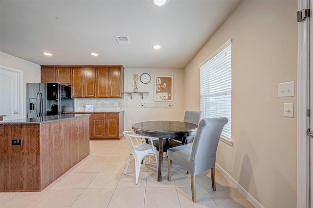 kitchen with decorative backsplash, black fridge, dark stone counters, a kitchen island, and light tile patterned flooring