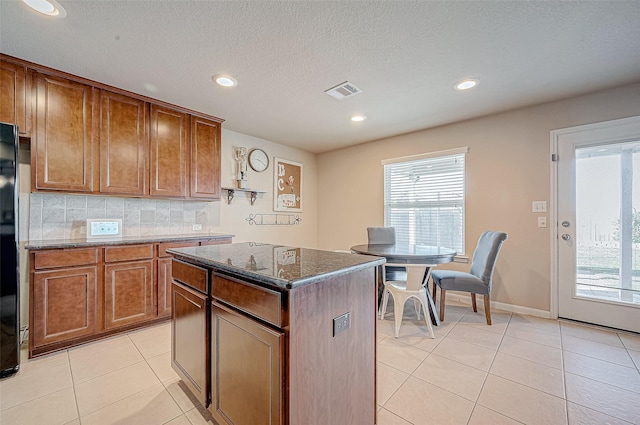 kitchen featuring backsplash, a center island, light tile patterned flooring, and dark stone counters