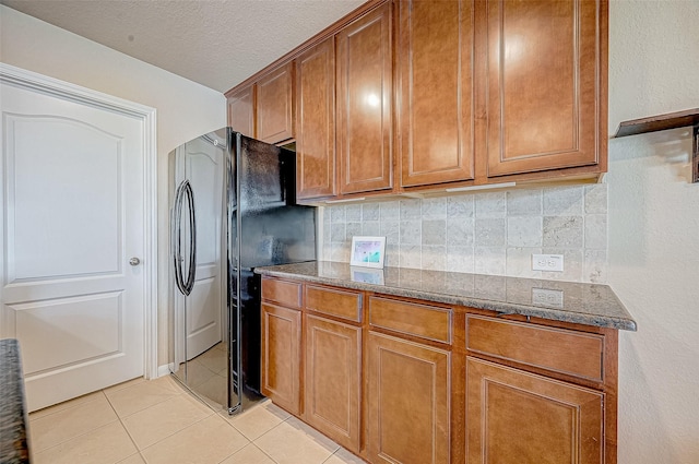 kitchen featuring black fridge, backsplash, dark stone countertops, a textured ceiling, and light tile patterned floors