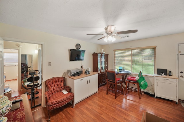 office space featuring light wood-style floors, a ceiling fan, a textured ceiling, and visible vents
