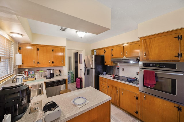 kitchen featuring brown cabinetry, backsplash, appliances with stainless steel finishes, light countertops, and under cabinet range hood