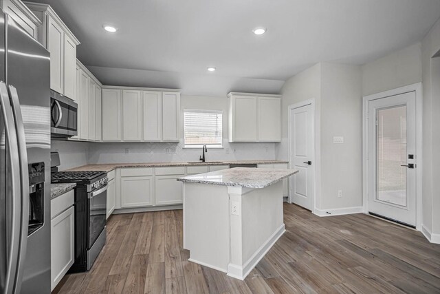 kitchen with sink, light stone countertops, appliances with stainless steel finishes, a kitchen island, and white cabinetry